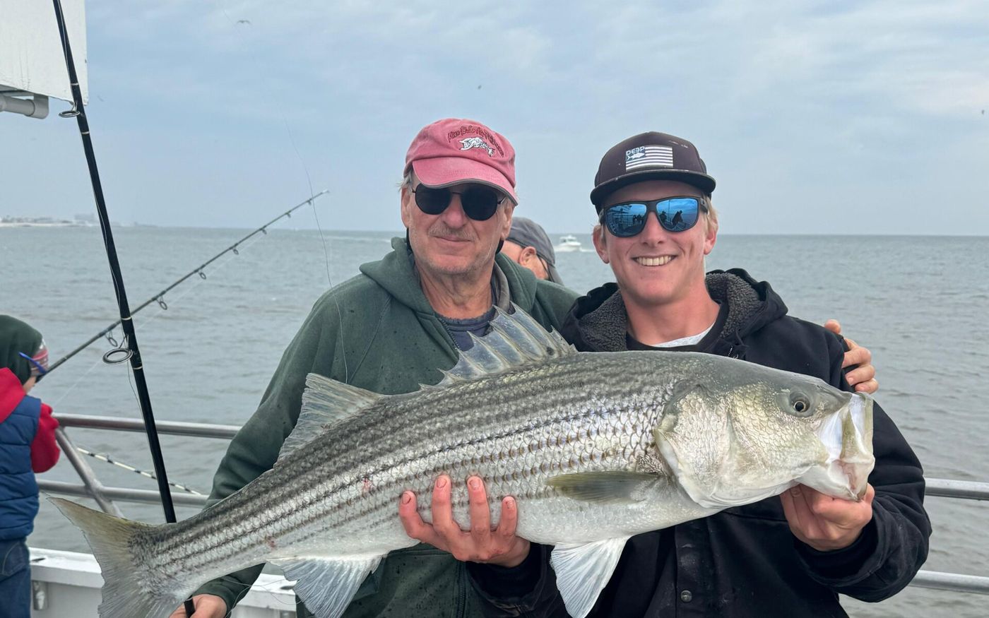 Two anglers holding a striped bass aboard the Miss Belmar
